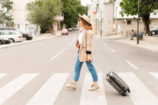 Девушка-туристка везет чемодан по пешеходному переходу